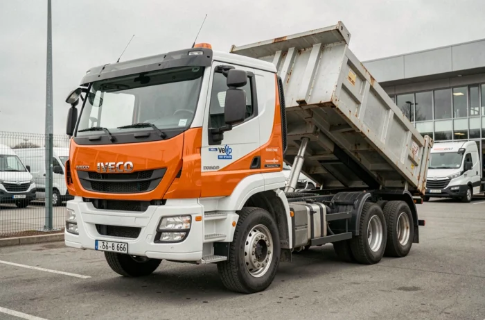 Camion benne Iveco neuf garé dans un parc de concessionnaire avec carrosserie orange et blanche visible de face